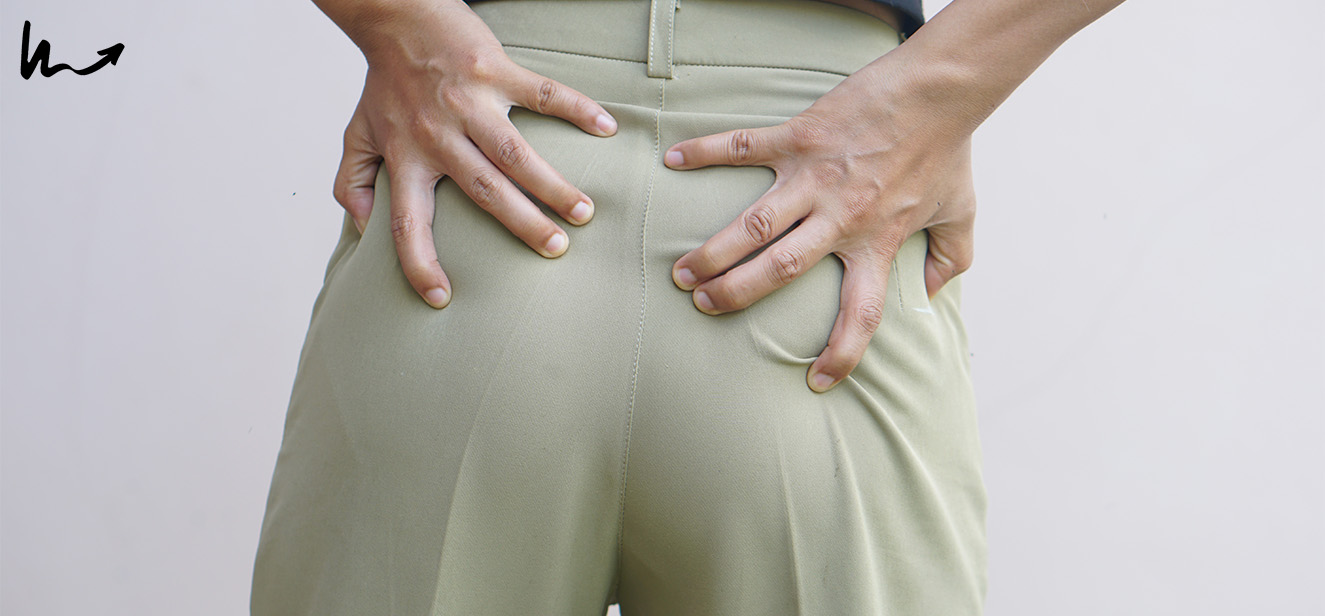 Woman experiencing buttock pain from poor posture at her desk.